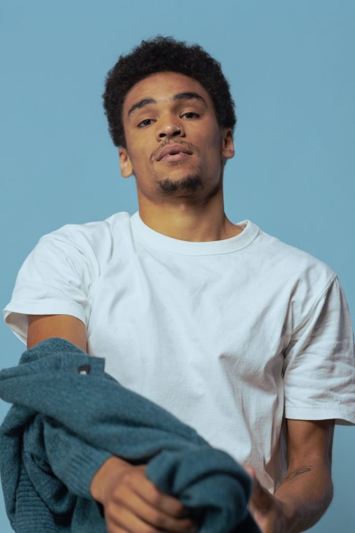 Young man with curly hair in a casual outfit against a blue background.